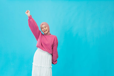 A joyful woman with her fist raised high in celebration against a vibrant blue backdrop