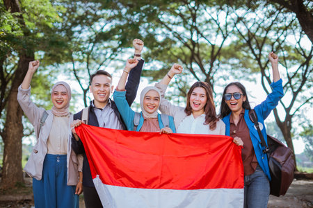 young students standing and holding indonesian flag with raised fist in outdoorsの写真素材