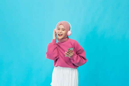 A joyful young woman listens to music with headphones while using her smartphone.