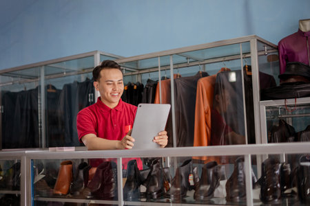 leather shoe salesman wearing red polo shirt holding tablet with smiling faceの写真素材