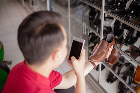 back view of male businessman taking picture of brown leather shoes using smartphoneの写真素材
