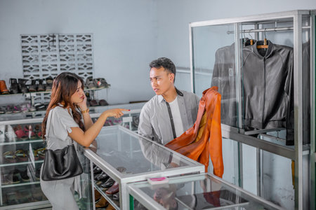 unhappy male staff serving female customer shopping leather jacket at storeの写真素材