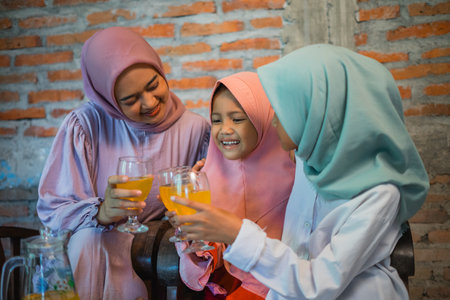 Asian mother and two daughters enjoy a drink together during Eid celebrationの写真素材