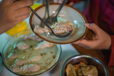 Closeup of hands serving a savory chicken dish at a communal meal enjoyed by allの写真素材