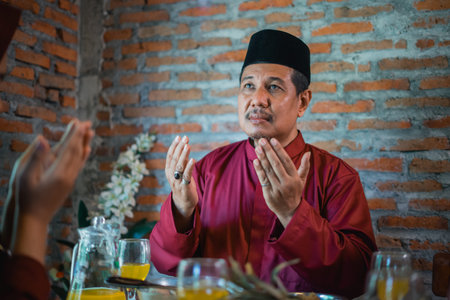 father in turban prays before eating with a Muslim family at the dining table during a celebration