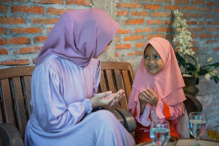 Asian Muslim mom teaches little girl to pray while sitting at homeの写真素材
