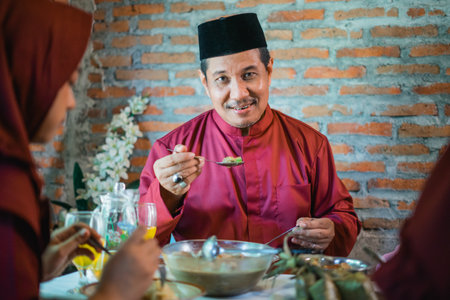 a father eats at the dinner table with family during Lebaran celebration at homeの写真素材