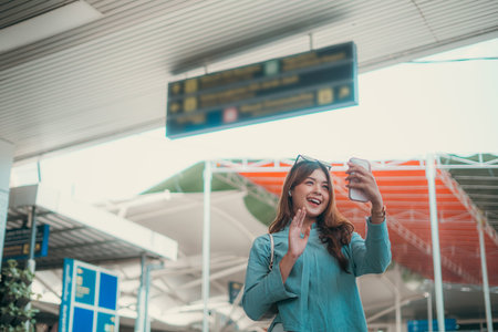 A cheerful woman who is engaging in a lively video call while at the busy airport terminal