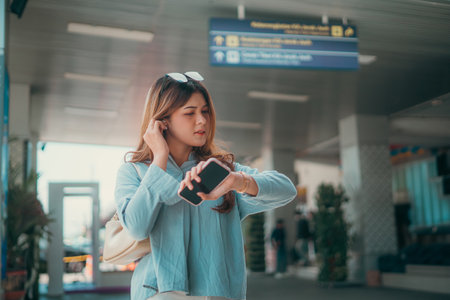 A young woman is intently looking at her smartphone while patiently waiting at an airport terminalの写真素材