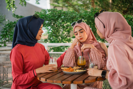 Three friends share snacks and drinks, enjoying quality time at a sunny cafの写真素材