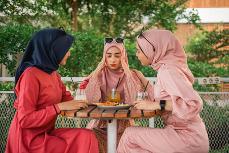 Women in hijabs joyfully discuss over drinks at an outdoor cafe in a vibrant atmosphereの写真素材