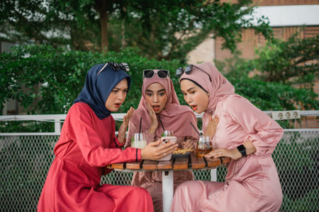 Three women in vibrant attire huddle around a device, sharing a moment of surprise.の写真素材