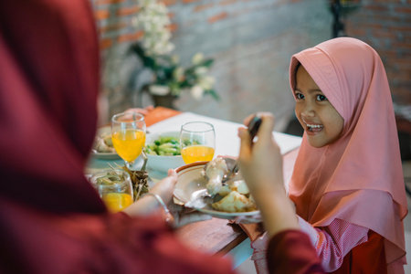 A joyful young girl smiles during a family meal, showcasing happiness and connection.の写真素材