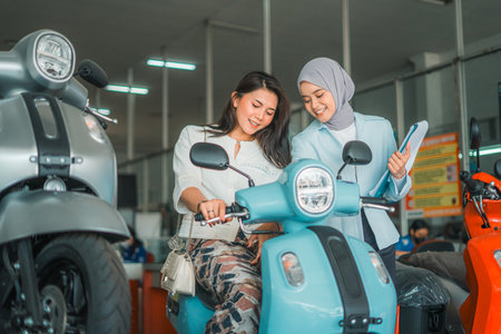 young woman trying out a new motorcycle with a veiled saleswoman at a showroomの写真素材