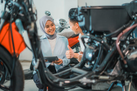 veiled shop assistant using a laptop serves buyers while looking at motorcycles in a showroom