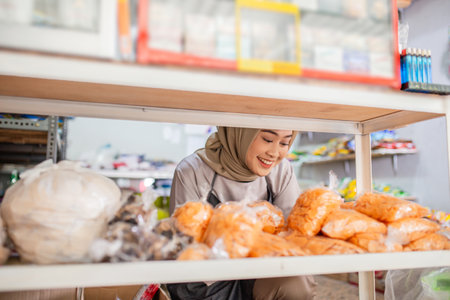A cheerful shopkeeper carefully organizing various goods in her welcoming grocery storeの写真素材