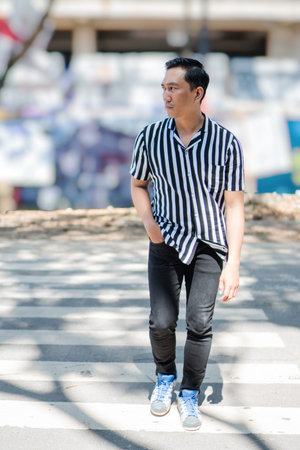 A trendy and fashionable young man is casually strolling through a lively urban setting