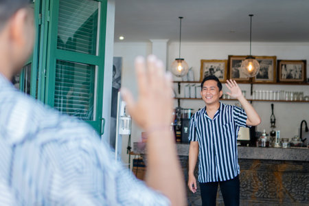 As two individuals meet at the entrance of a cozy cafe, they exchange a warm greetingの写真素材