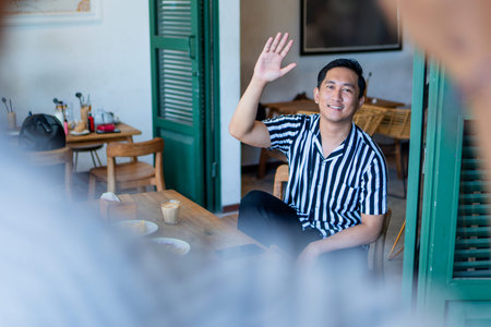 A young man waves cheerfully in a caf, showcasing a warm, friendly atmosphere