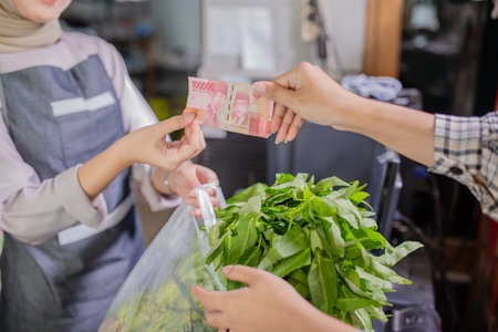 A financial transaction is happening in a busy market where a consumer is buying fresh greensの写真素材