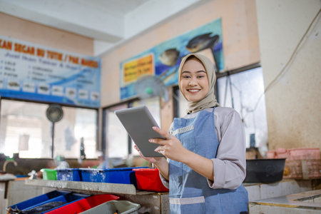 In a vibrant and bustling market setting, a smiling woman wearing an apron holds a tablet tightly
