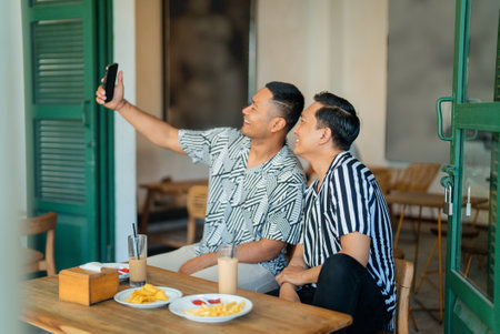 Two friends enjoying breakfast together, capturing a fun selfie in a cozy settingの写真素材