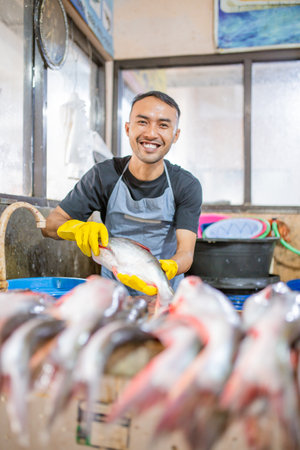 A cheerful fishmonger smiles brightly while showcasing a variety of fresh fish at the marketの写真素材