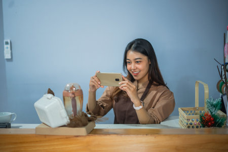 female shop assistant takes a photo of a gift ordered by a customer using a cell phone at her shop.の写真素材