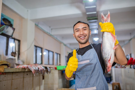 In a bustling and lively market, a cheerful fishmonger proudly showcases a variety of fresh fishの写真素材
