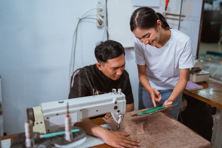 asian male tailor paying attention to the digital tablet that showed by the female production crew at window treatments production houseの写真素材