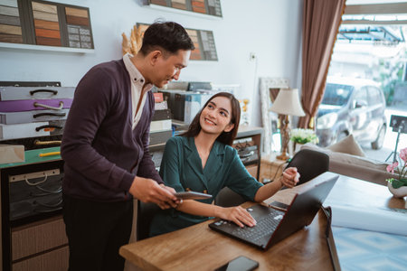 couple of asian interior shop crew looking each other while doing their job with the laptop and digital tablet at interior shopの写真素材