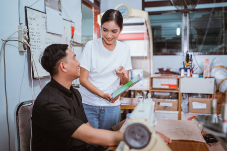 beautiful asian employee pointing on the green screen digital tablet while showing it to the male tailor at window treatments production houseの写真素材