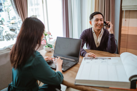 asian male customer calling on phone while sitting in front of the female shopkeeper that operating the laptop at interior shopの写真素材