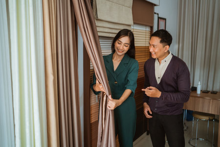 beautiful asian shopkeeper showing the curtain fabric sample to the asian male customer at curtain shopの写真素材