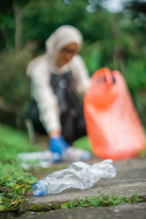 blurred picture of woman collects waste and focus on plastic bottle junk in outdoor backgroundの写真素材