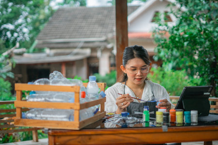 asian woman coloring recycled plastic bottle with acrylic paint
