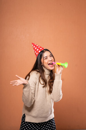 A joyful woman in a colorful party hat celebrates at a fun gathering with a whistleの写真素材