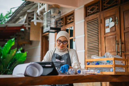 hijab woman watching tutorial on tablet while crafting plastic bottle, recycle conceptの写真素材