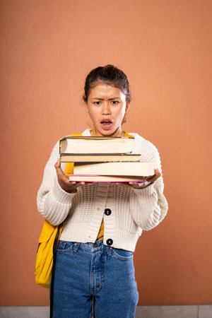 A diligent student struggles with a heavy stack of books while navigating her dayの写真素材