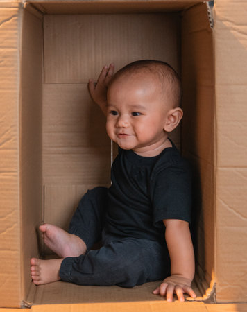 A joyful and smiling toddler is happily sitting inside a large cardboard box, playingの写真素材