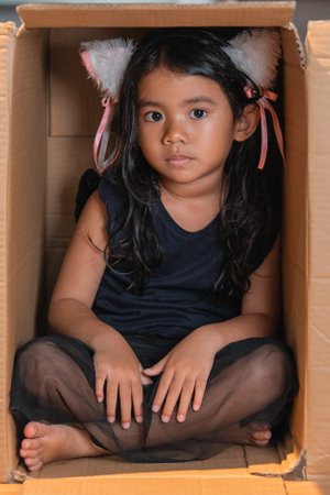 A girl in black clothing sits in a cardboard box, wearing cute cat ears on her headの写真素材