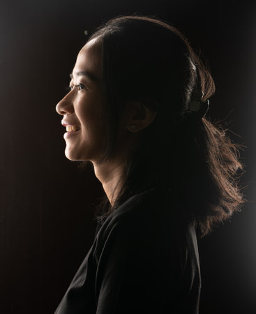 A charming and artistic side profile of a joyful woman captured in soft and gentle lightingの写真素材