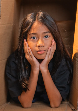 A child sits in a cardboard box, gazing thoughtfully into the distance, lost in thoughtの写真素材