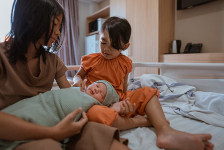 Sisters lovingly interact with their newborn sibling in a cozy home environment.の写真素材