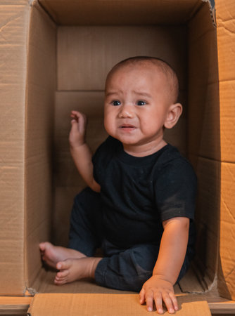 A baby is sitting inside a cardboard box, showcasing a very candid emotional momentの写真素材