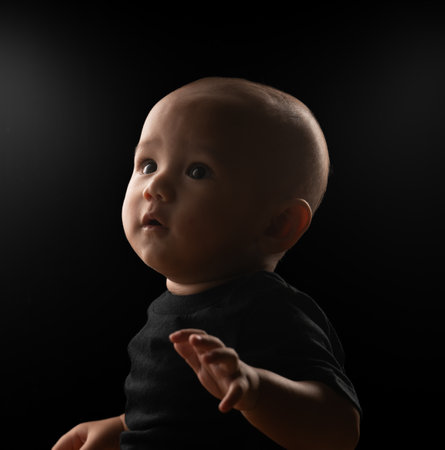 A curious baby gazes upward, captured in dramatic lighting against a dark backdrop.の写真素材