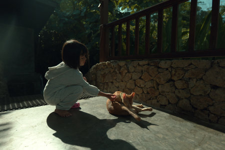 A young child gently pets a fluffy cat that is basking in the warm and inviting sunlightの写真素材