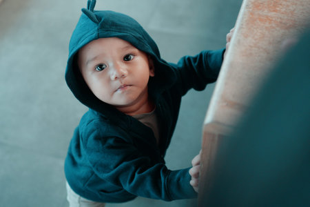 A cute child in a green hoodie exploring a vibrant indoor space with colorful furnitureの写真素材