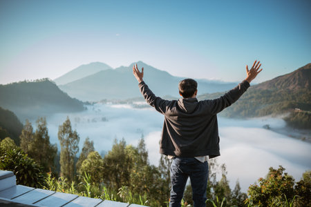 A man stands triumphantly atop a majestic mountain, his arms outstretched wide, embracing the vast...