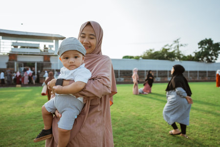 In a beautiful field under the vast sky, a woman is gently holding a baby in her arms, surrounded by grass and treesの写真素材